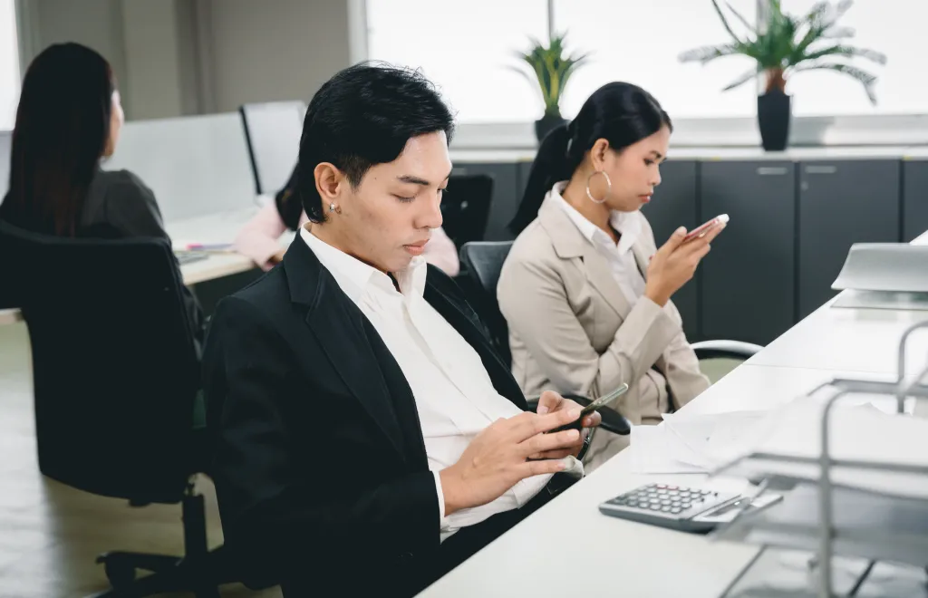two employees scrolling on smartphone instead of working